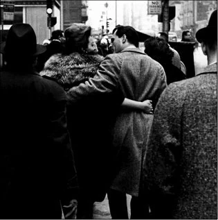 Street photograph: a couple walking arm in arm in a crowd